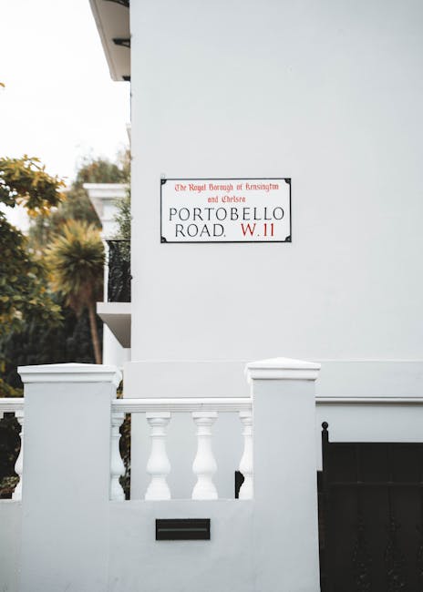 The image depicts a small brick building with a grey tiled sloped roof, located on a quiet street. In front of the building, there is a concrete sidewalk with a black waste bin positioned near the cur